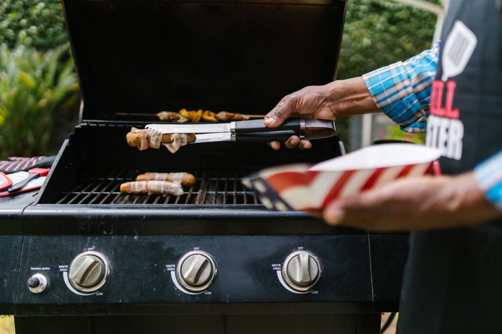 Person grilling hotdogs wrapped in bacon outdoors. Perfect for summer barbecue and celebration themes.