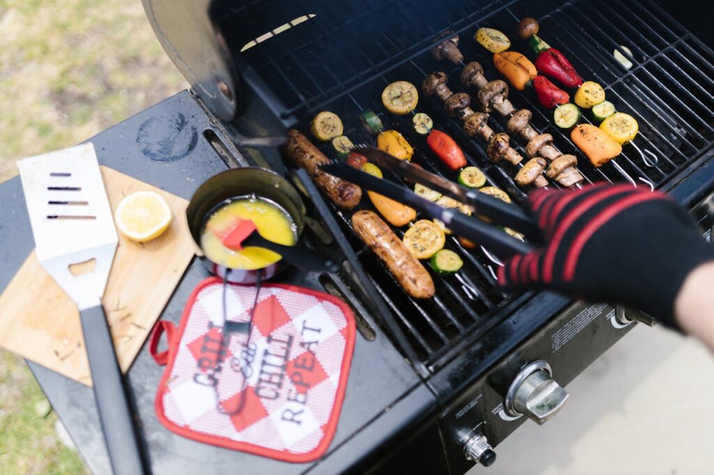Colorful grilling scene with sausages, veggies, and grilling tools on a barbecue.